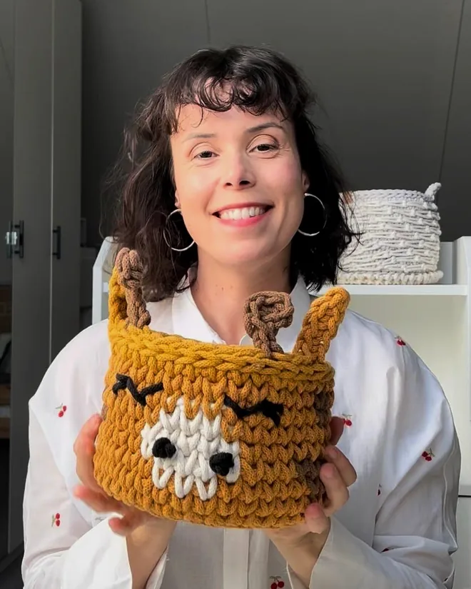 Fruzsi, smiling, holding up a mustard giraffe basket she made.
