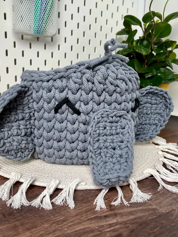 A grey crochet elephant basket with round ears and a trunk hanging over the front