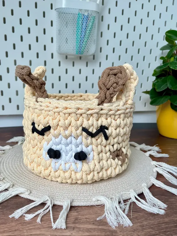 A butter yellow crochet giraffe basket with sleepy eyes, a white muzzle and two brown horns